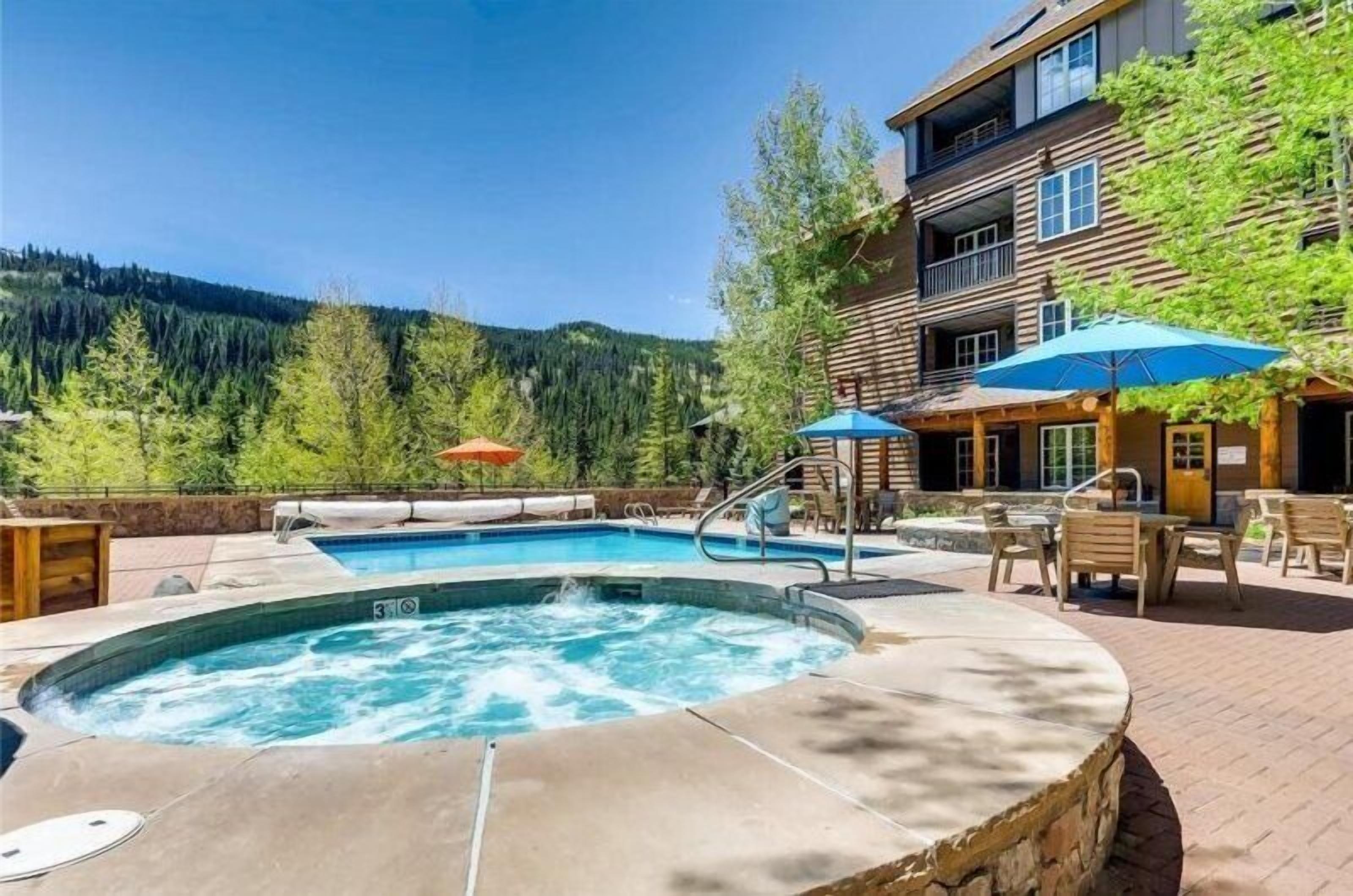 Un bain à remous entouré de meubles de jardin et d’une piscine, avec une vue sur les montagnes en arrière-plan.