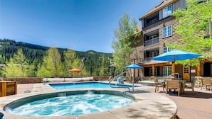 A hot tub surrounded by outdoor seating and a pool, with a mountain view in the background.
