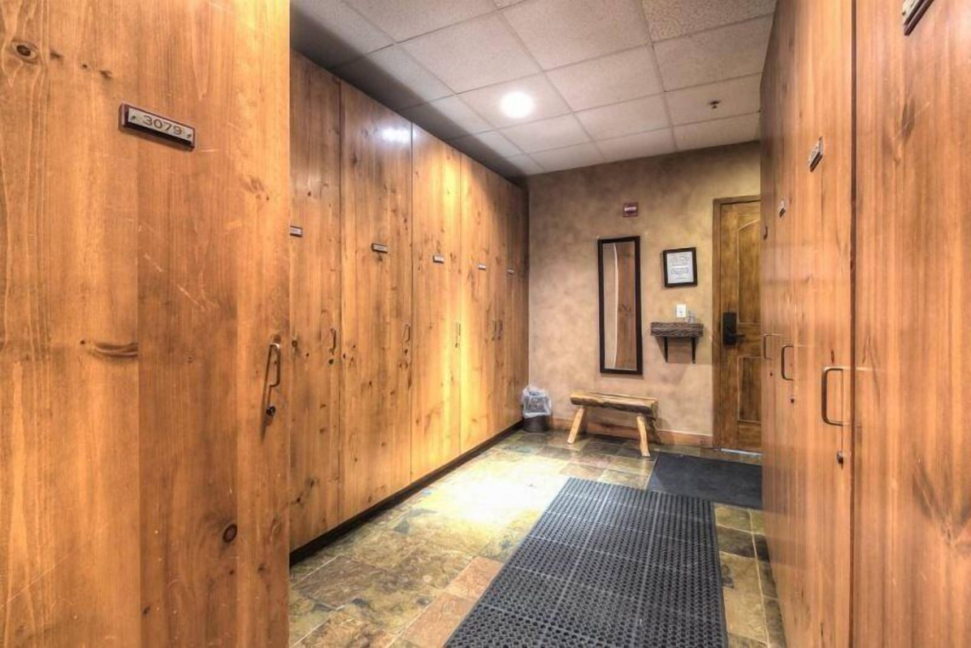 A hallway with wooden lockers, a bench, and a tiled floor.