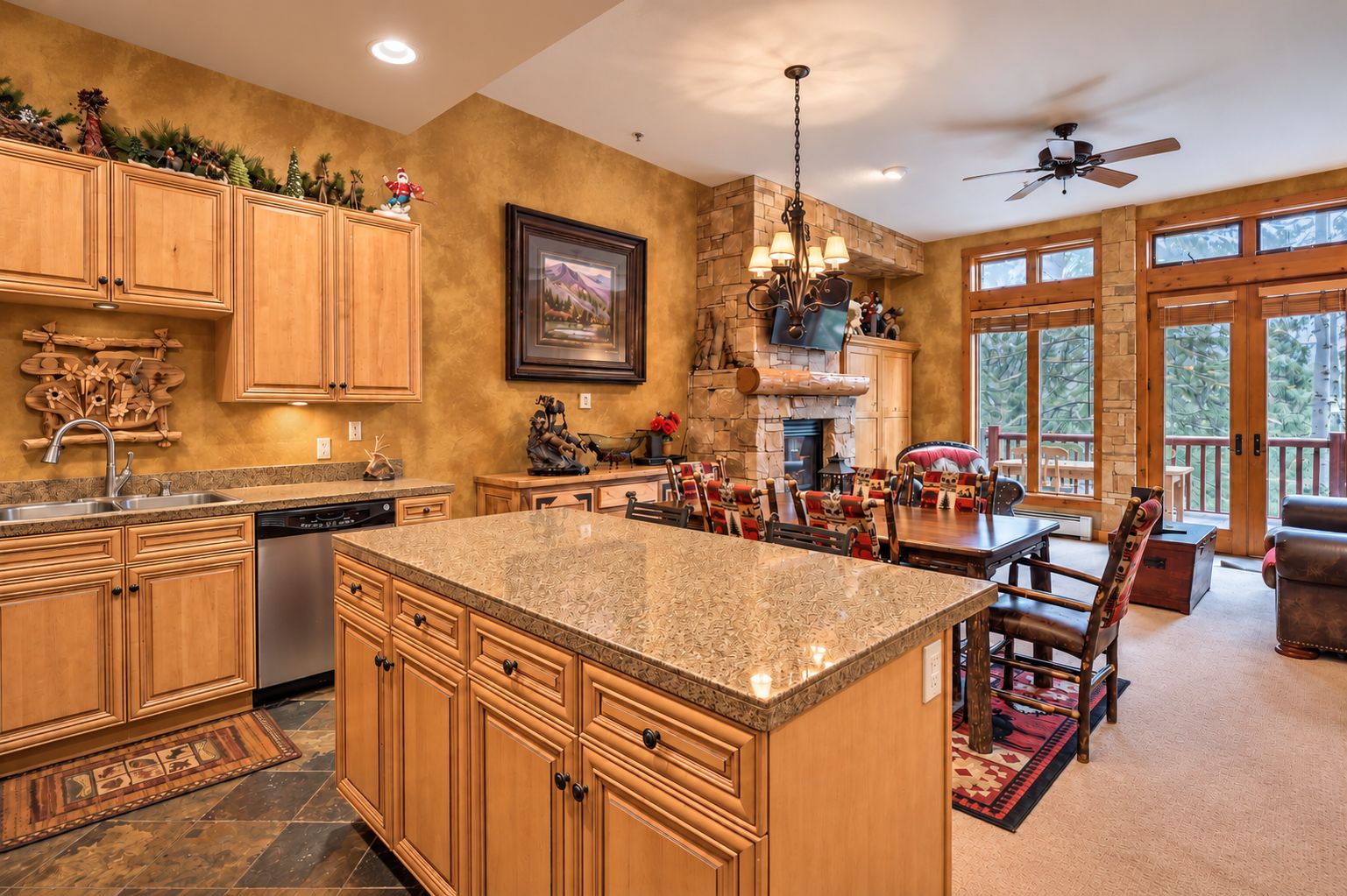 A spacious kitchen with a large island, wooden cabinets, and a stone fireplace.