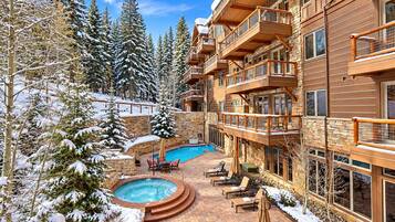 A multi-story building with a pool area, outdoor seating, and snow-covered trees.