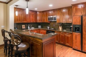 A kitchen with wooden cabinets, a granite countertop, a built-in microwave, and a refrigerator.