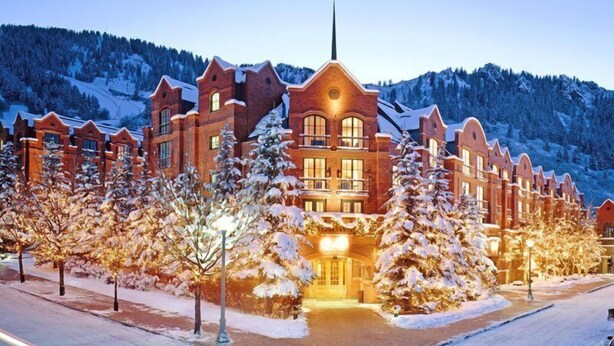 A large, multi-story hotel with a prominent central building and symmetrical wings, surrounded by snow-covered trees and a mountainous backdrop.