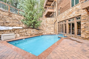A stone-walled pool with a wooden deck and a stone building with large windows.