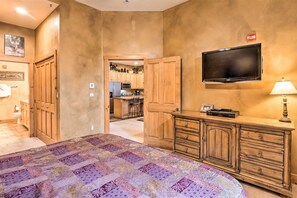 Un dormitorio con una cama grande, un armario de madera, televisión y una kitchenette al fondo.
