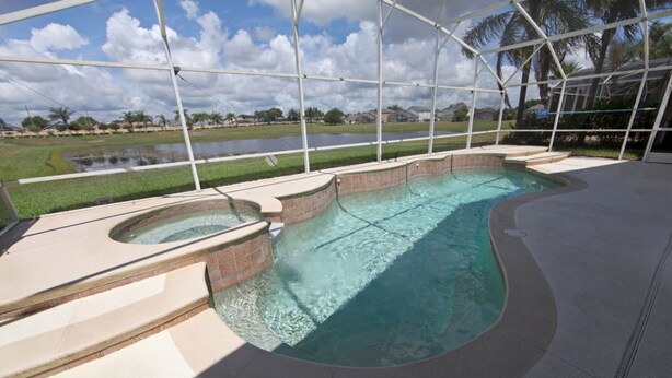 A swimming pool with a curved design, surrounded by a covered area with a view of a grassy field and a body of water. - 3BR 2BA Home in Rolling Hiils by CV-2616 (Kissimmee)