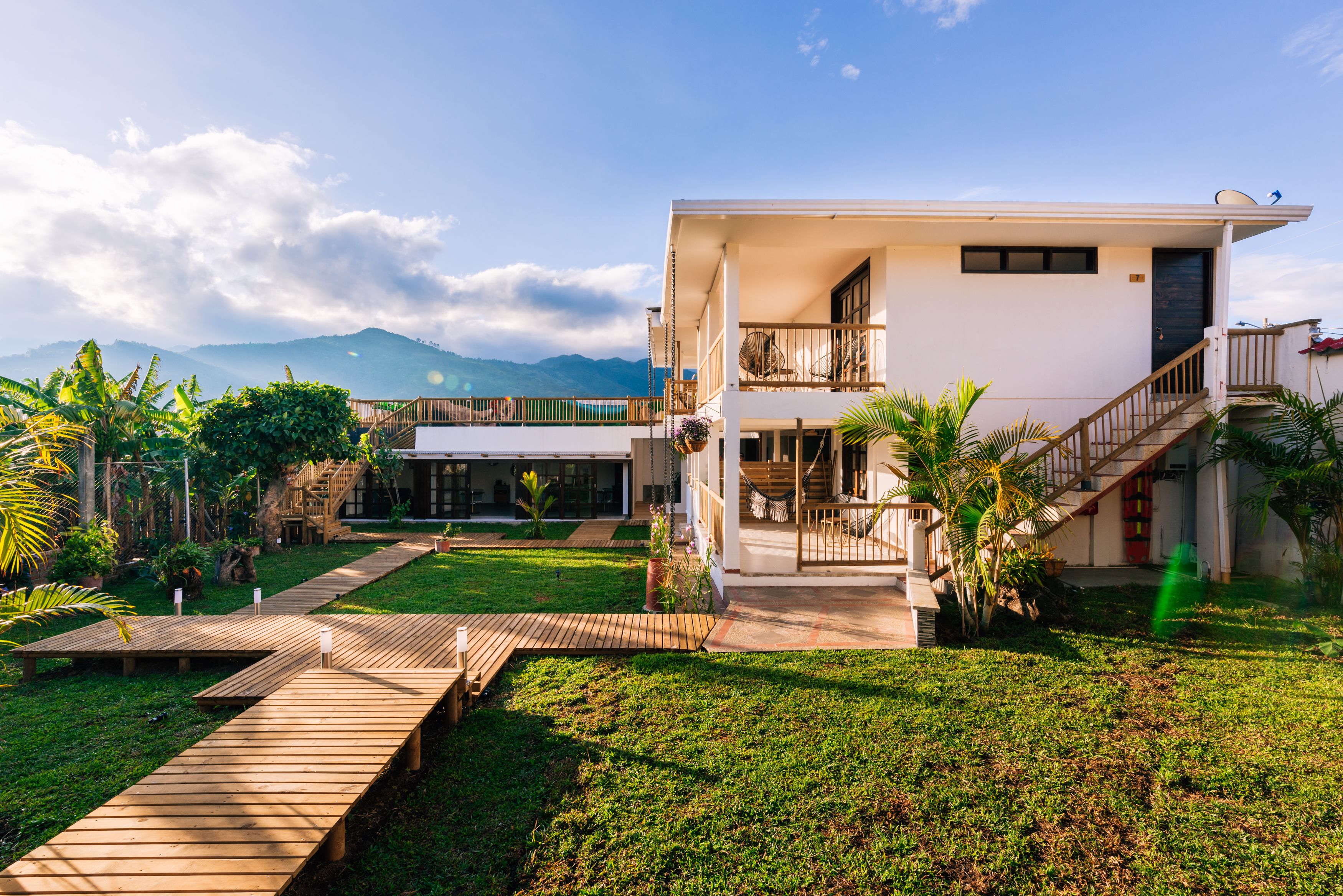 A modern house with a spacious backyard, a wooden deck, and a staircase leading to a balcony.