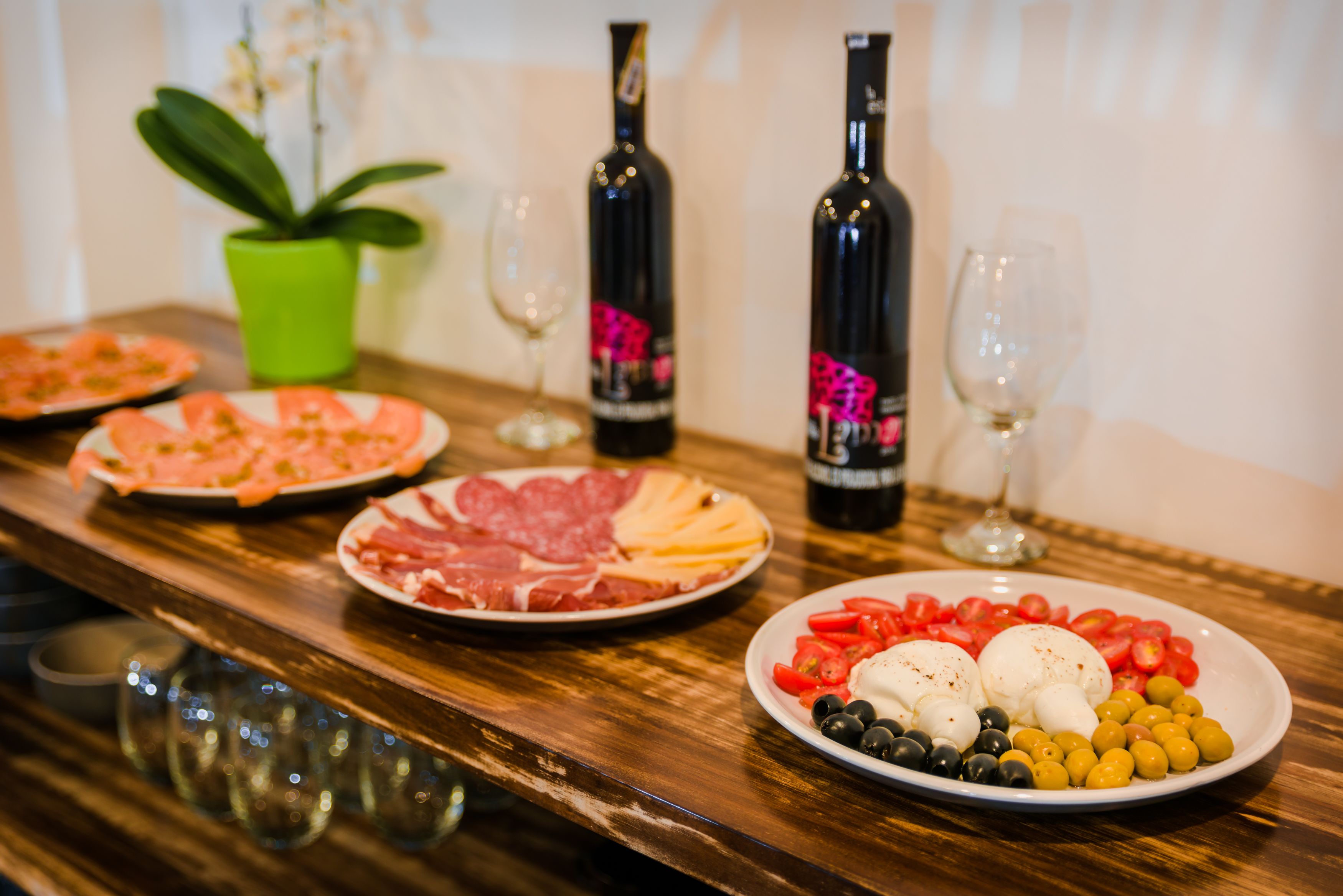 Un tavolo di legno con piatti di cibo, bottiglie di vino e bicchieri.
