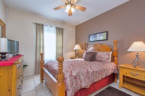 A bedroom with a wooden bed, two bedside tables with lamps, a television on a dresser, and a ceiling fan. - 3BR 2BA Home in Windsor Palms by CV-8168 (Kissimmee)