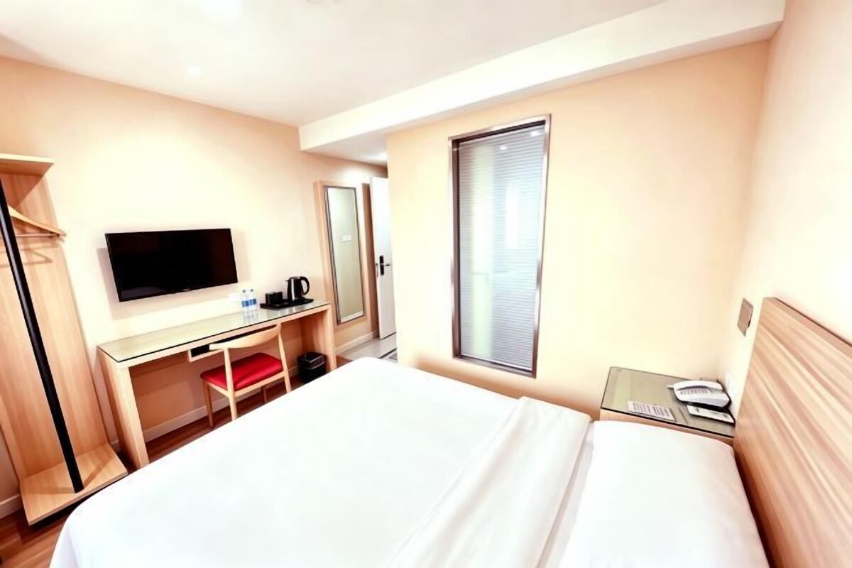 Habitación de hotel con cama, escritorio, televisor, espejo y ventana.