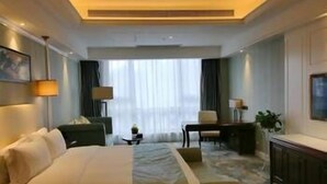 Une chambre d’hôtel avec un grand lit, un bureau, une chaise et une fenêtre avec des rideaux.