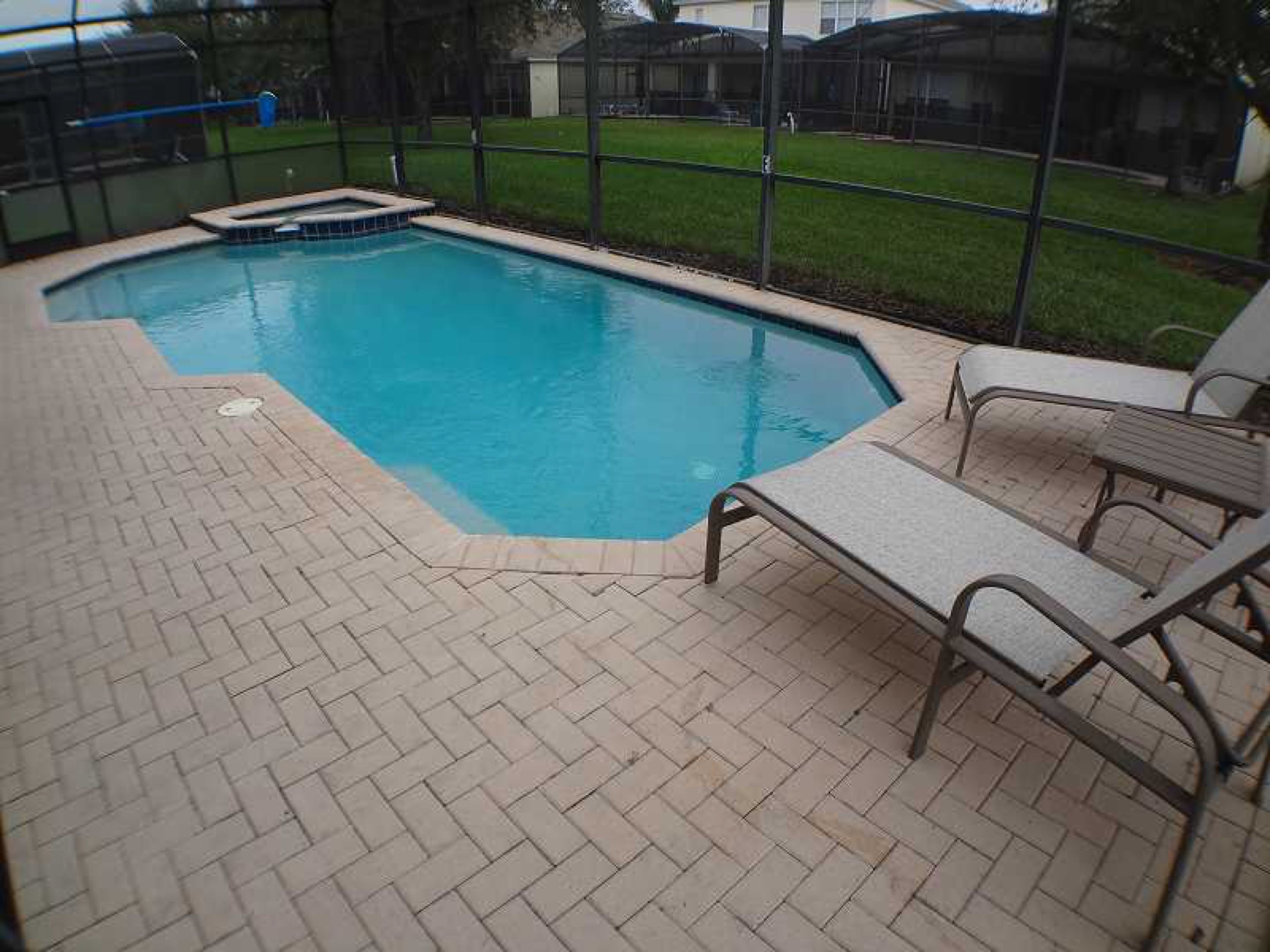 A rectangular swimming pool with a tiled deck and two lounge chairs.