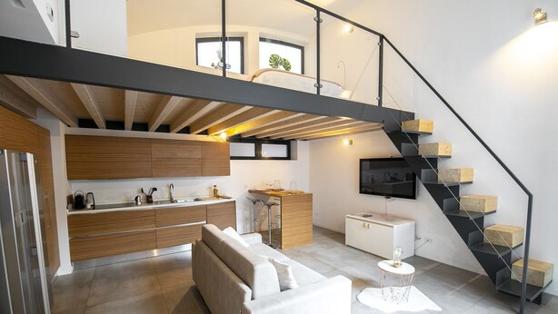 A modern kitchen with wooden cabinets, a built-in oven, and a dining area with a white table and chairs. - Design Central Apartment (Bergamo)