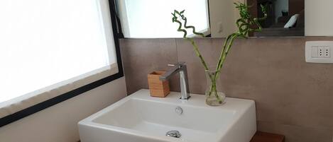 A bathroom with a white sink, a wooden box, and a bamboo plant in a glass vase.