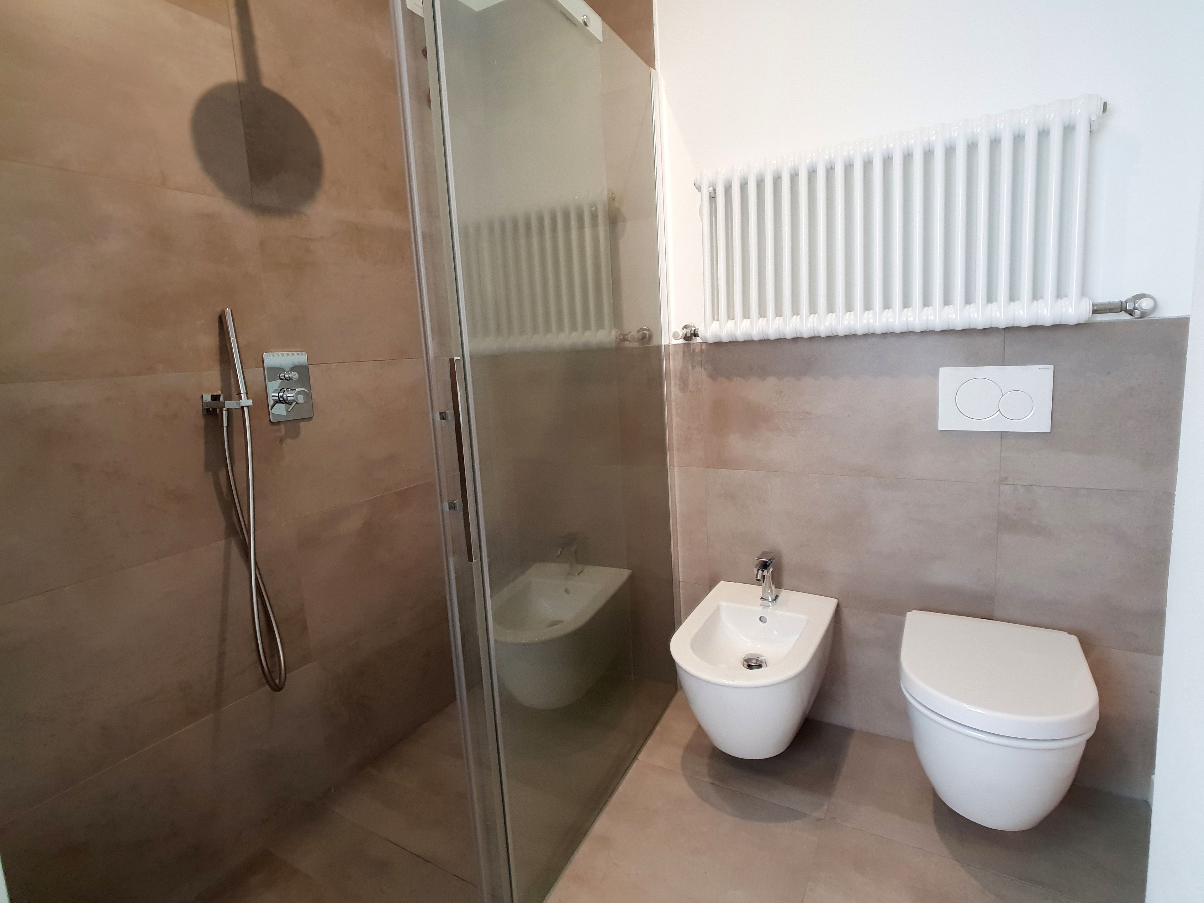 A bathroom with a glass shower enclosure, a bidet, and a toilet.