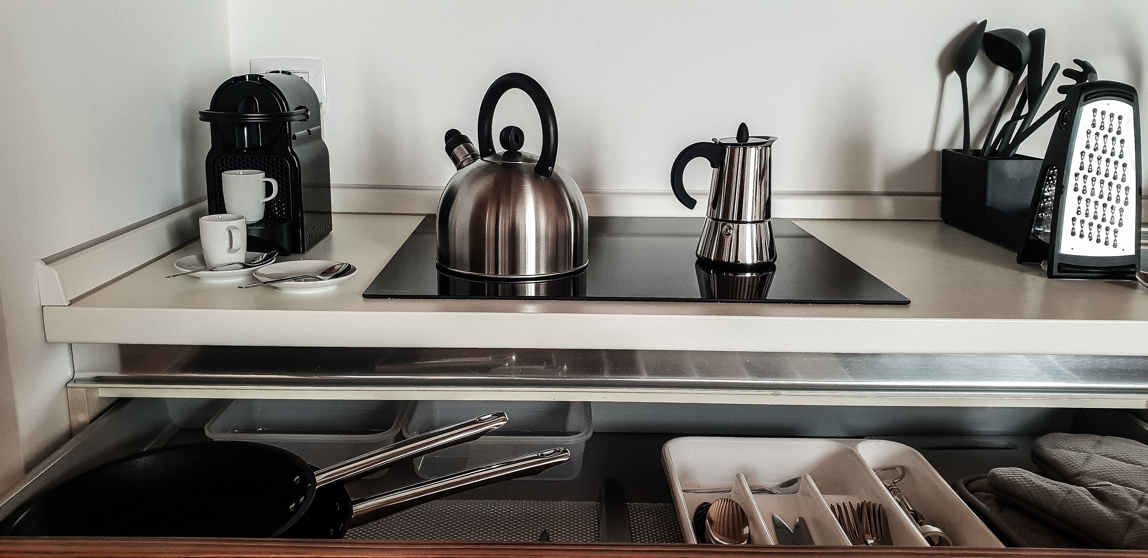 A kitchenette with a coffee maker, kettle, and a set of utensils.