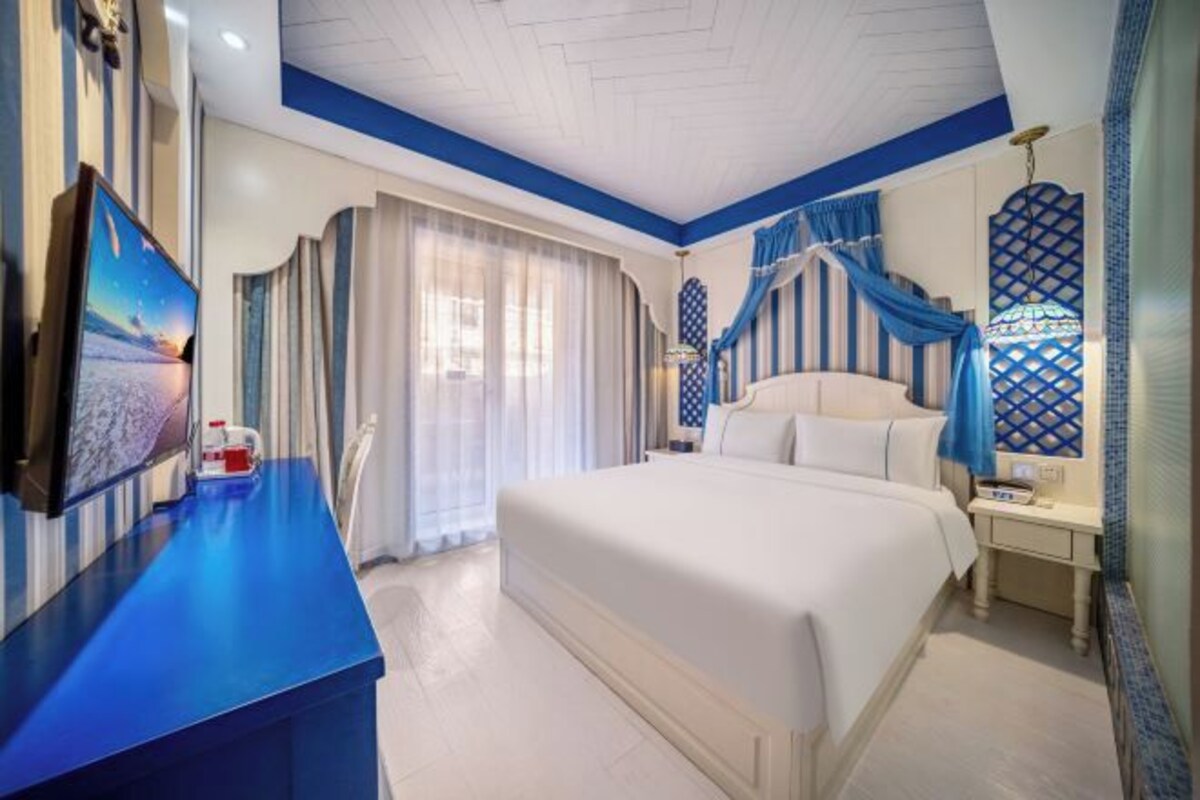 Une chambre d’hôtel avec un grand lit, un téléviseur à écran plat, une table de chevet et une fenêtre avec des rideaux.