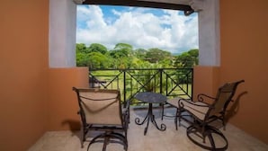 A balcony with two chairs and a small table, overlooking a green landscape with trees and a clear sky. - Los Suenos Resort Veranda 6C (Jacó)