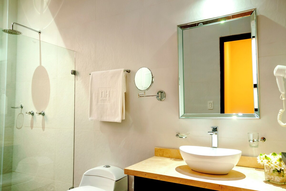Un baño moderno con ducha de vidrio, un espejo grande, un lavamanos blanco y una toalla colgada en la pared.
