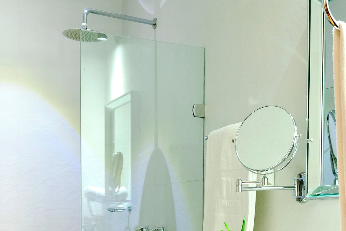 Un baño moderno con ducha de vidrio, inodoro blanco, lavamanos y espejo.