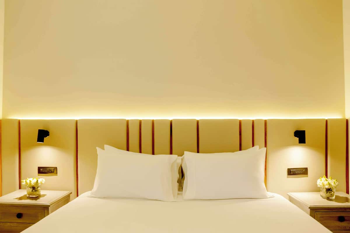 A hotel room with a large bed, two bedside tables, and a nightstand with a vase of flowers.