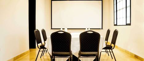 Una sala de conferencias con una pantalla grande, cuatro sillas y una mesa.