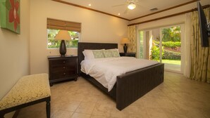 A bedroom with a bed, bedside tables, a bench, a ceiling fan, and a view of a garden through a sliding door. - Los Suenos Resort Veranda 3G  (Jacó)