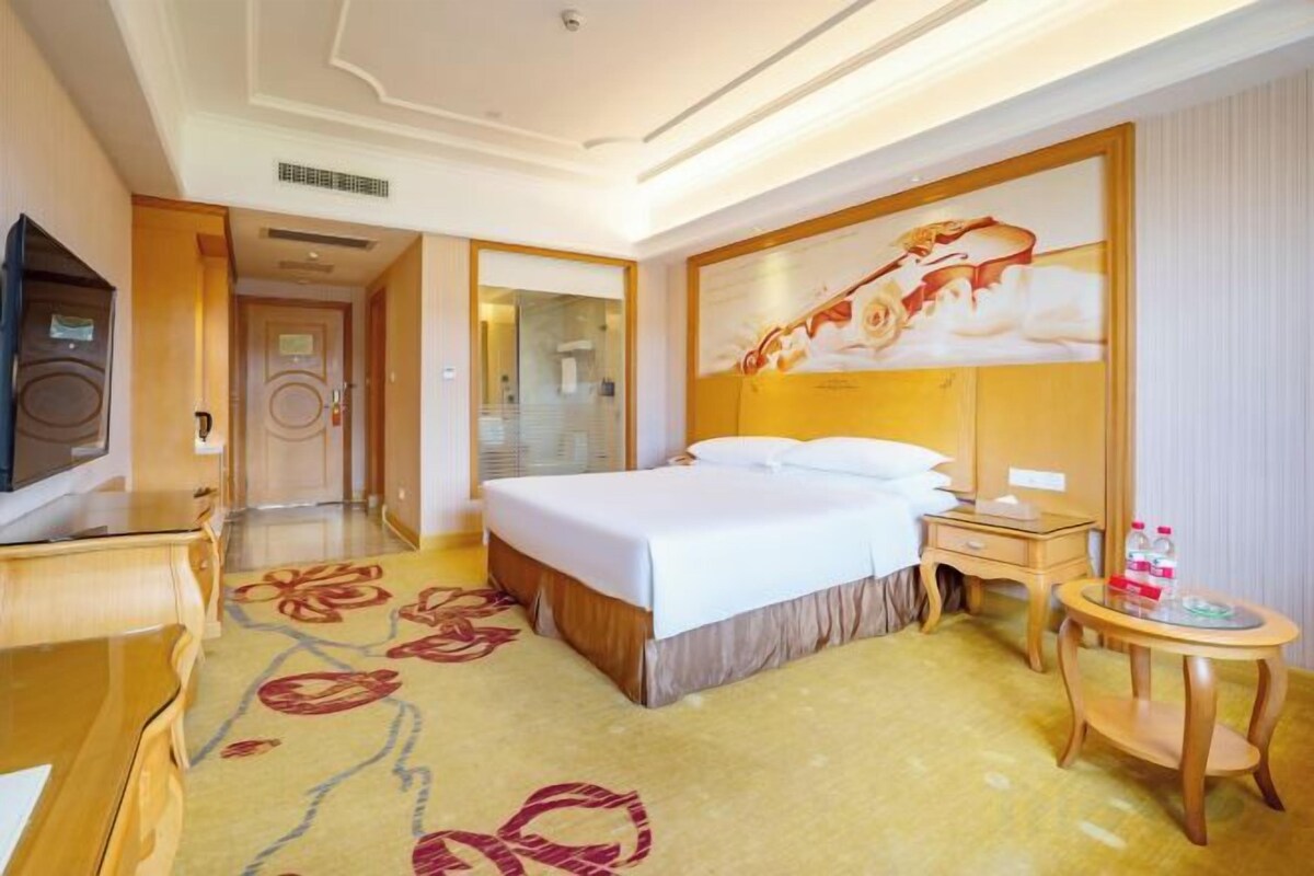 A hotel room with a bed, bedside table, lamp, and a television.