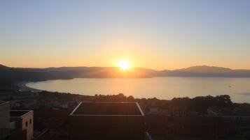 A coastal town at sunset with a view of the sea and distant mountains.