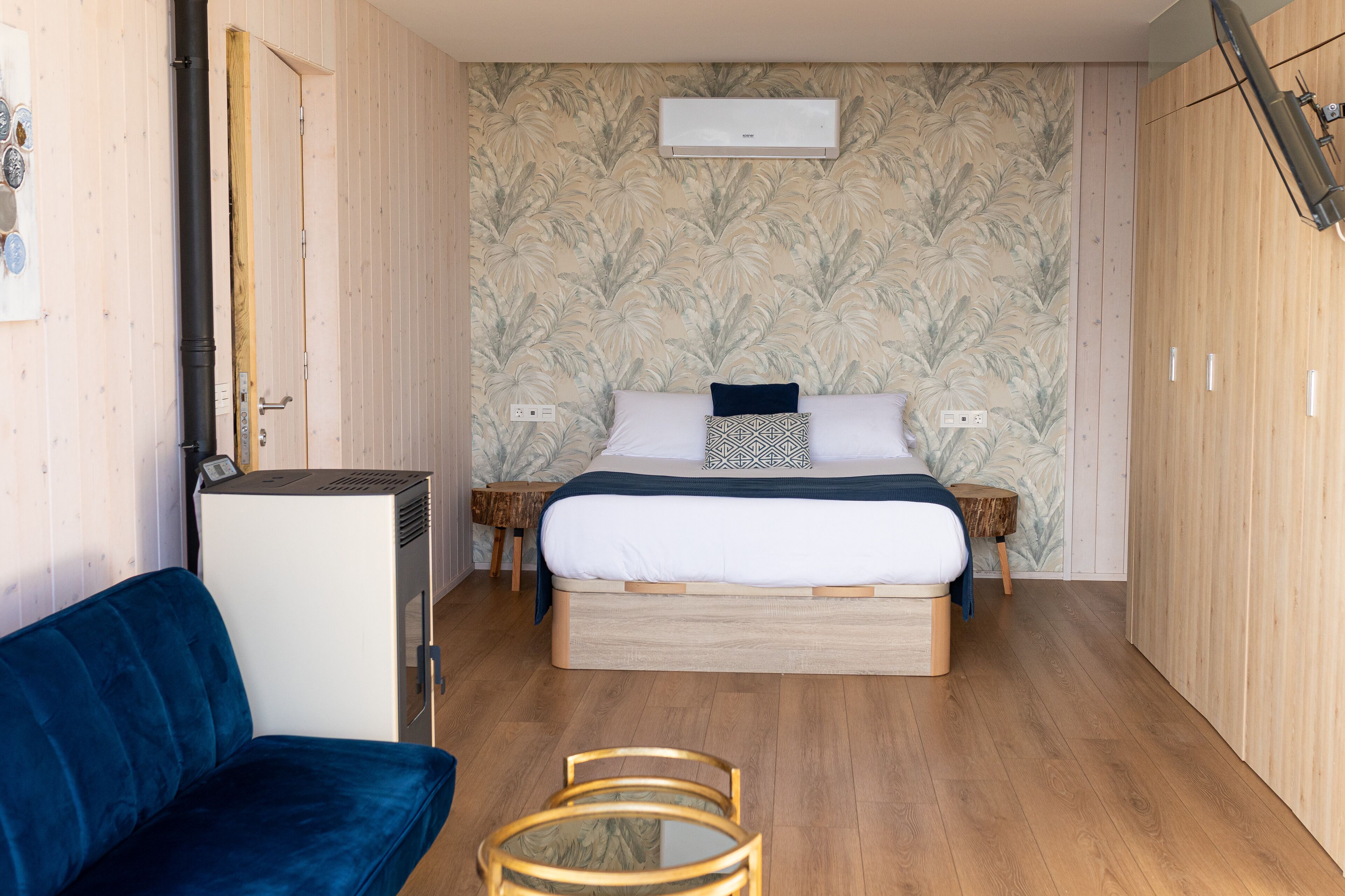Un dormitorio con una cama, un sofá azul, una mesita y un armario de madera.