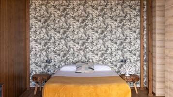 Un dormitorio con cama, paredes de madera, pared con textura y una pequeña mesa redonda con un objeto decorativo.
