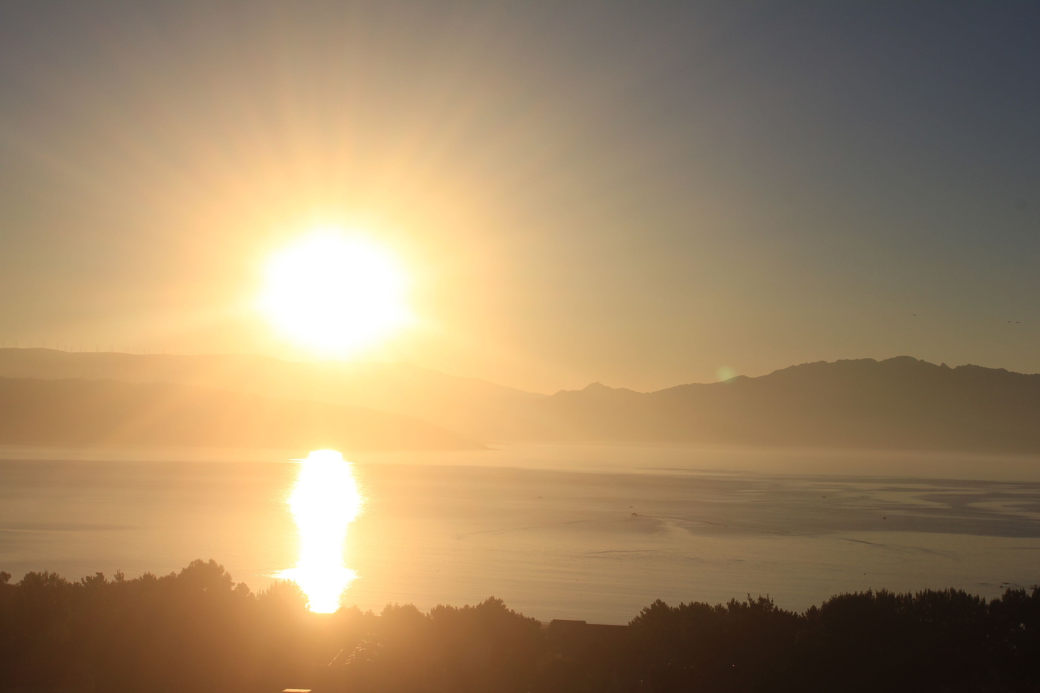 A sunrise over a calm body of water with mountains in the distance.