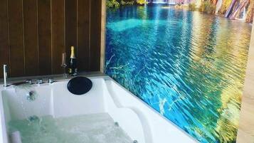 A jacuzzi with a waterfall mural, a bottle of champagne, and a glass on the side.