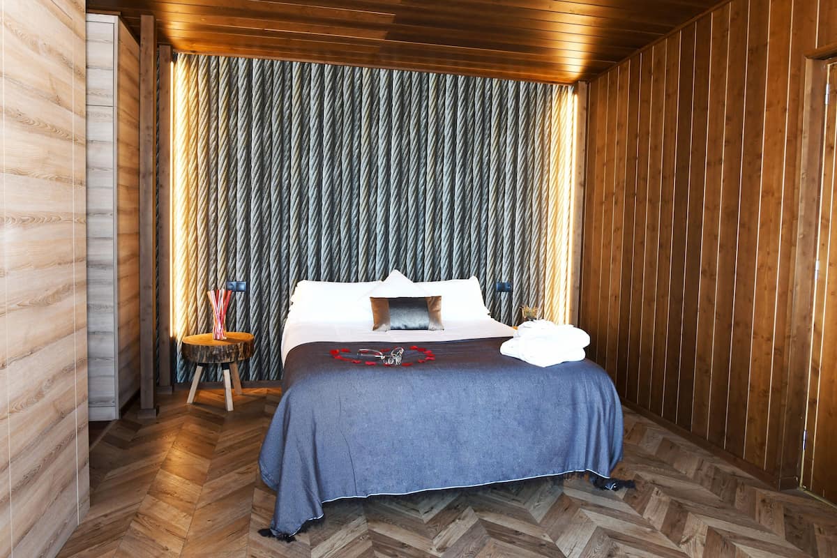 A room with a bed, wooden walls, a herringbone floor, and a curtain with a vertical pattern.