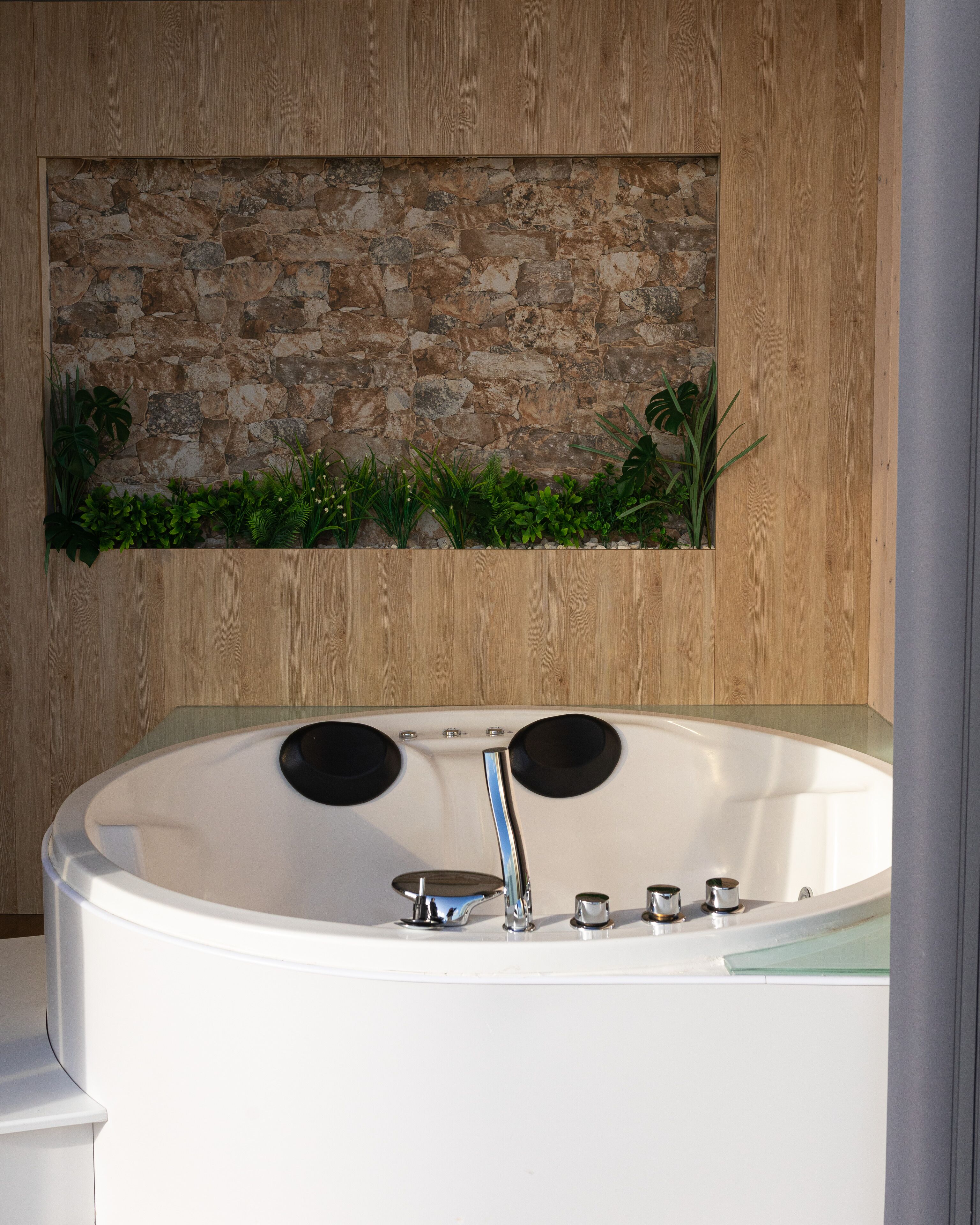 A modern bathroom with a stone wall, a wooden panel, and a bathtub with two black circular seats.