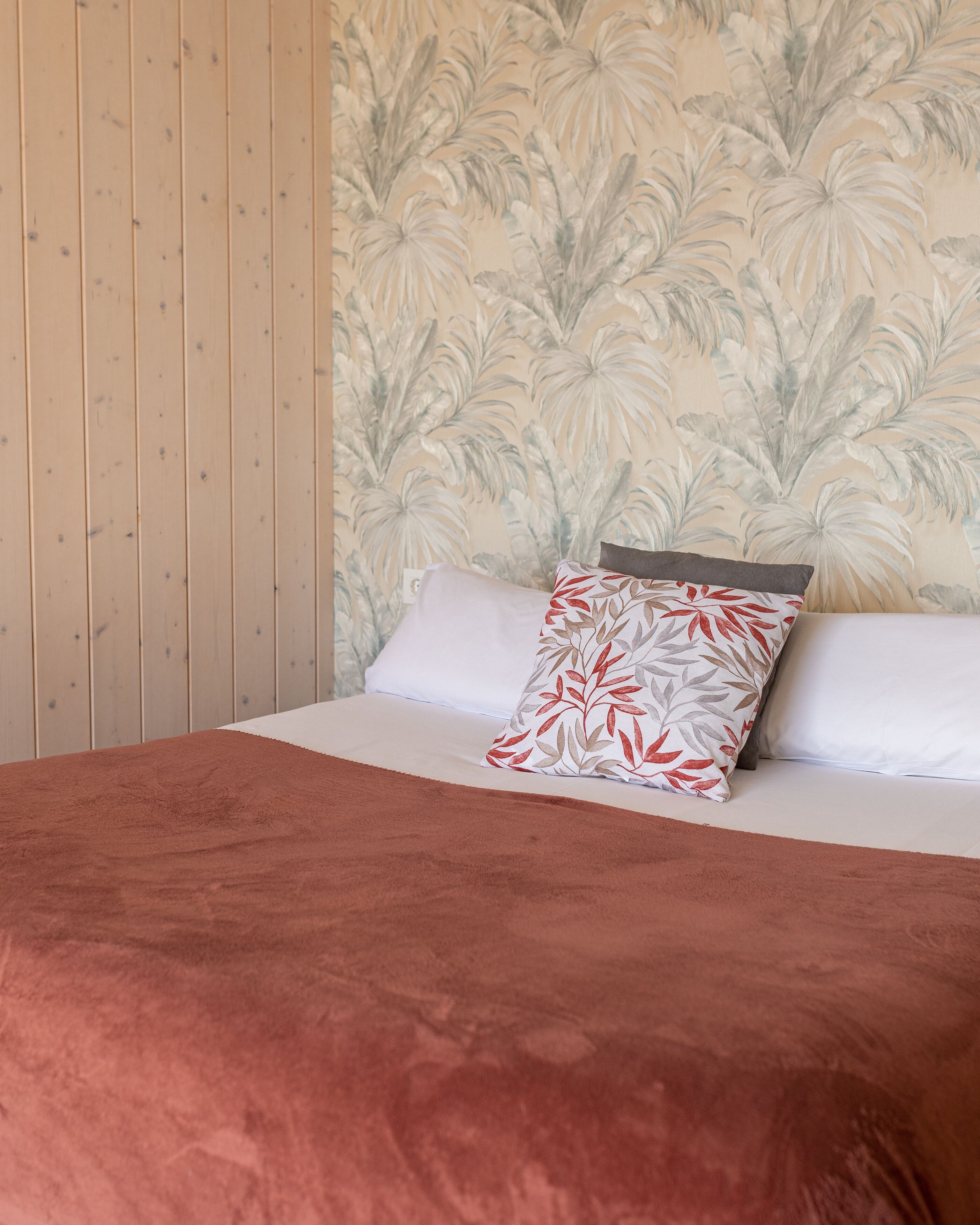 A bed with a red blanket, white pillows, and a floral-patterned pillow.