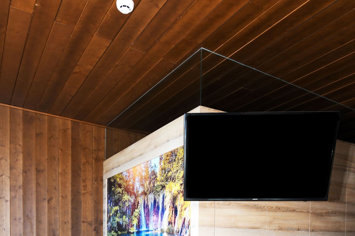 A modern bathroom with a wooden ceiling, a large bathtub, and a wall-mounted TV.