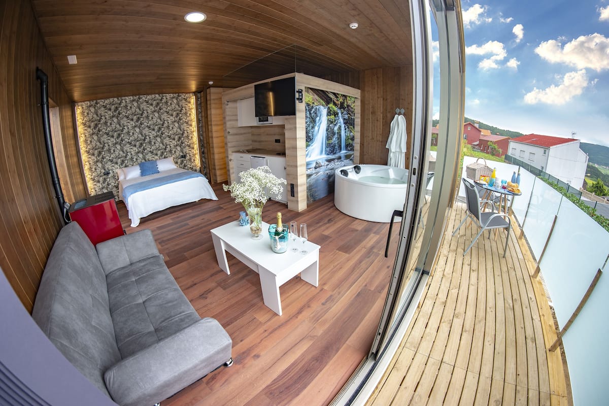 A modern interior with a sofa, a bed, a dining table, and a hot tub.