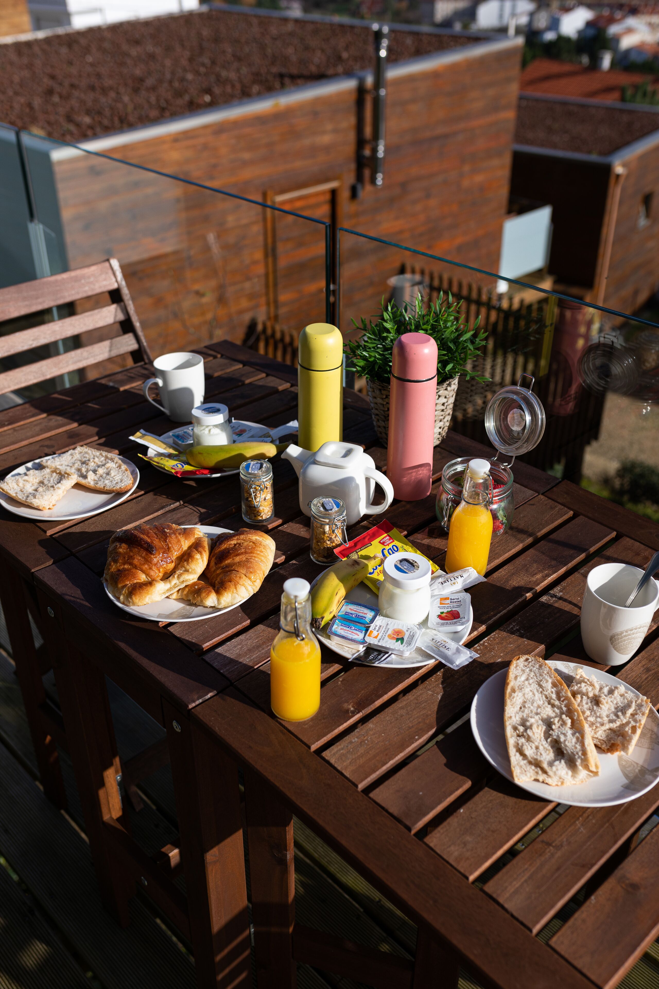 Una mesa de madera dispuesta con alimentos para el desayuno, como cruasanes, pan, jugo y café.