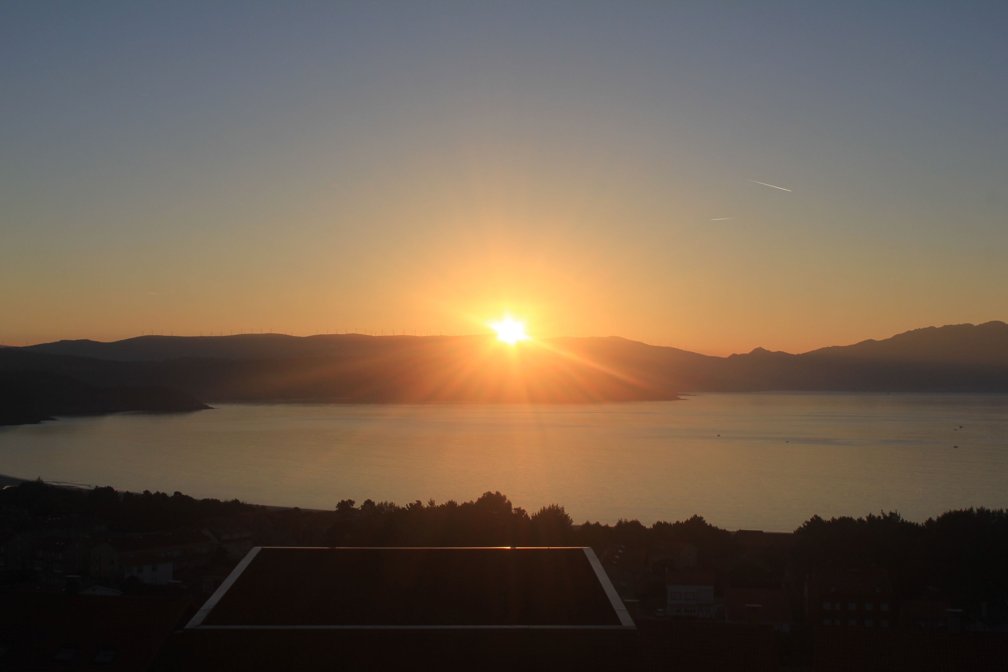 A sunset over a calm lake with mountains in the background and a silhouette of a building in the foreground.