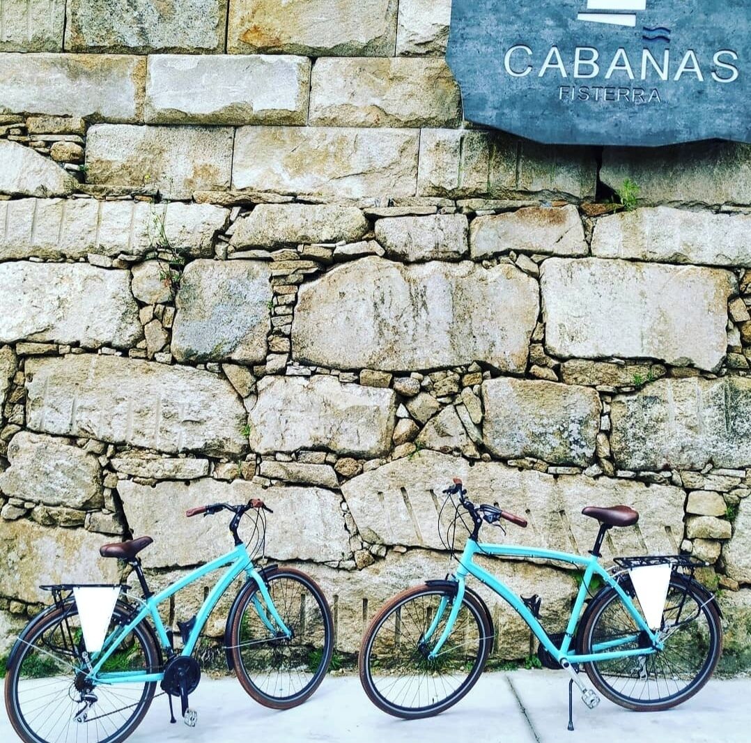 Two bicycles parked against a stone wall with a sign reading "CABANAS FISTERRA".