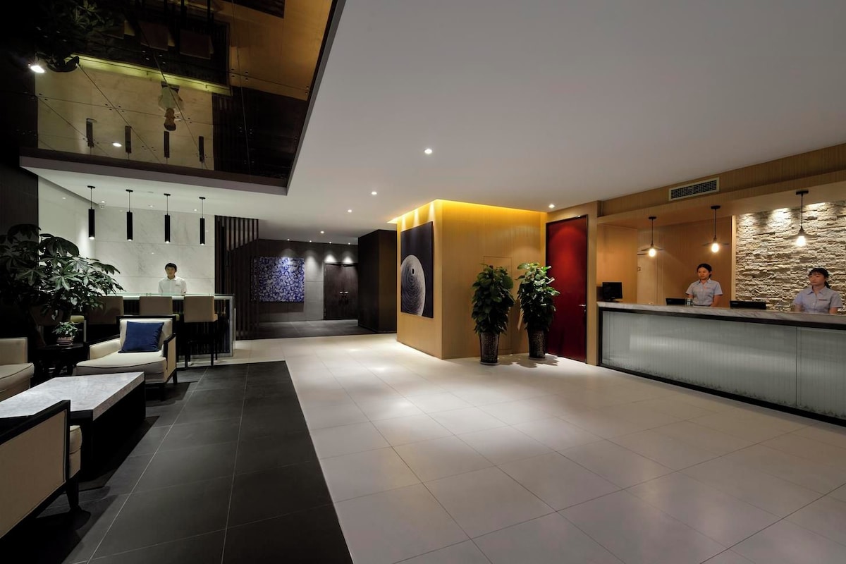 A modern hotel lobby with a reception desk, seating area, and a staircase leading to an upper level.