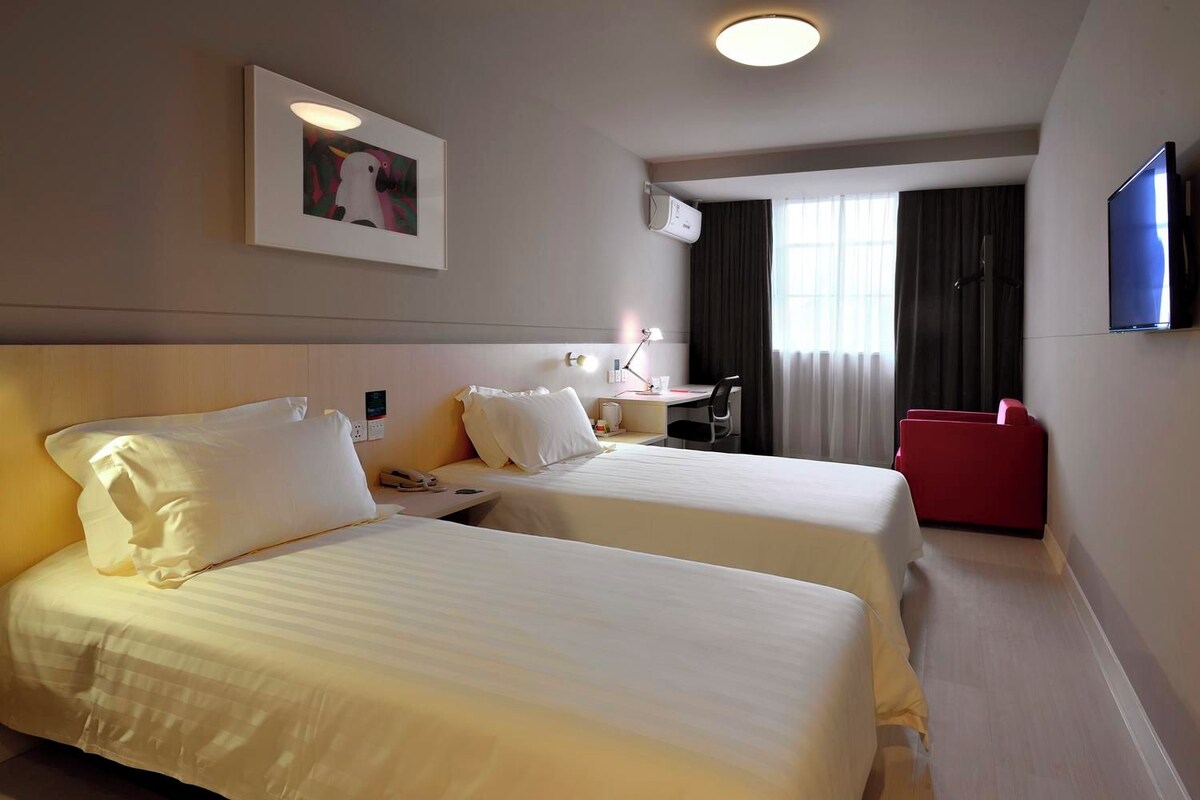 A hotel room with two beds, a desk, a chair, a TV, and a window with curtains.