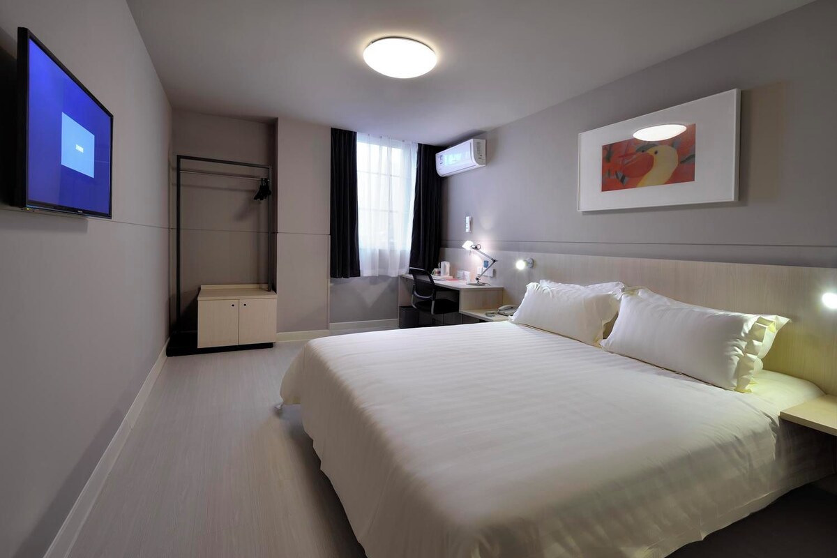 A hotel room with a bed, bedside table, desk, chair, and a TV mounted on the wall.