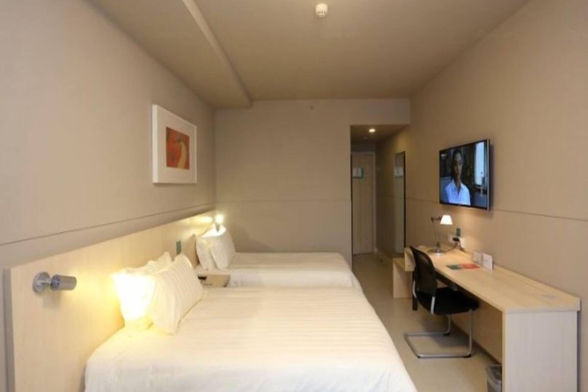 A hotel room with two beds, a desk, a chair, a TV, and a door leading to another room.