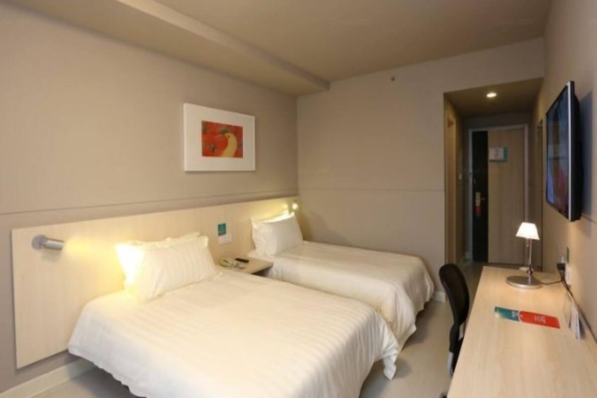 A hotel room with two beds, a desk, a chair, a TV, and a painting on the wall.