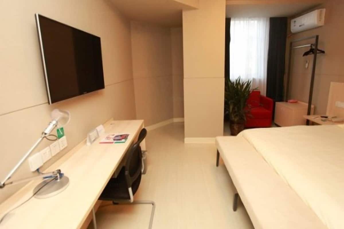 A hotel room with a bed, a desk with a computer, a TV, and a red chair.