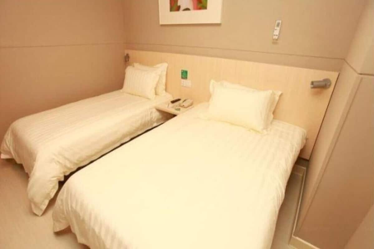 Two single beds with white bedding in a room with beige walls and a wooden headboard.