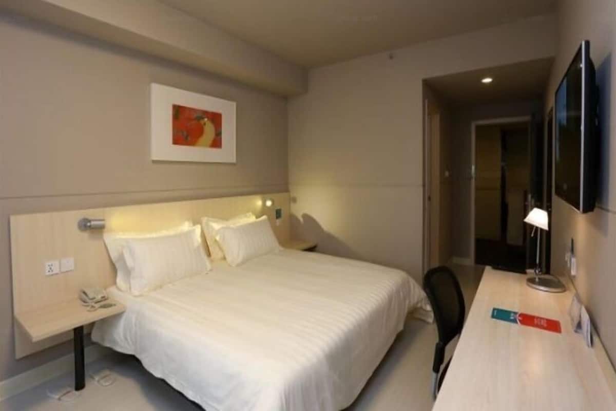 A hotel room with a bed, bedside table, lamp, and a painting on the wall.