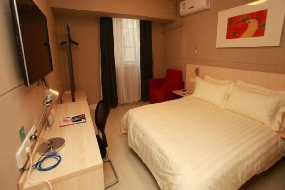 A hotel room with a bed, a desk with a computer, a chair, a TV, and a window with curtains.